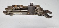 Stacked vintage metal open-end wrenches secured by a rusted metal clasp, showing wear and light rust