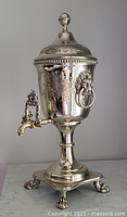 Full front view of silver-plated tea urn with lid on and spigot extended, showing overall shape and condition.