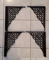 Four cast iron brackets laid out in two rows on a tiled floor, showing size and shape
