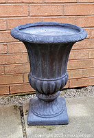 Front view of the grey concrete planter urn with fluted body and ornate detailing, square base visible.