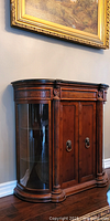 Front view of wood credenza with two central doors and curved glass side cabinets beneath gold-framed wall art