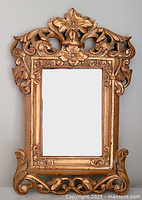 Front view of ornate gilt wood mirror showing detailed floral and scroll carving and rectangular reflective glass.