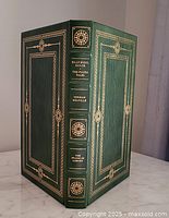 Front and part of spine of a green leather bound book with gold decorative borders and title on spine