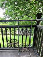 Full view of the 47-inch rusted metal planter standing on a deck railing with green outdoor background visible.