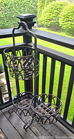 Front view of the tall metal plant stand showing the top and two bottom circular planter holders and the decorative bell.