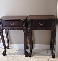 Pair of dark wood carved side tables, front view, showing decorative legs, claw feet, and drawer with metal handle
