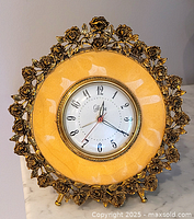 Front view showing clock face, yellow ring, and detailed rose-shaped gold-tone metal frame.