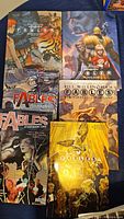 Top view shows five Fables comic books arranged on a dark surface, each with illustrated colorful covers featuring characters and titles.