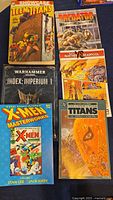 Photo of six comic and graphic novel books showing covers of Showcase Teen Titans, Predator, Warhammer 40K, Panther Deadpool, X-Men Masterworks Vol 1, and New Teen Titans.