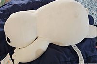 Photo showing side view of the white Baymax plush lying horizontally on dark blue fabric, visible tag attached