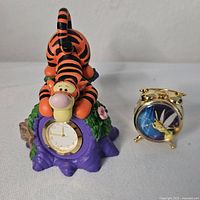Both mini clocks together, featuring Tigger on a purple base and a small gold-tone Tinkerbell alarm clock.