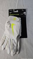 Front view of new Nike Huarache Edge batting glove in white with yellow swoosh, attached to original card, size XL indicated.