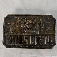 Front view of vintage rectangular Rolls Royce belt buckle showing embossed classic car and figures design with text 'ROLLS ROYCE SPRINGFIELD MASS'.