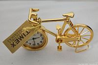 Close-up angle showing gold-tone bicycle clock with Timex tag attached to handlebar and visible clock face in front wheel.