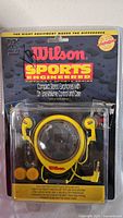 Front view of unopened vintage Wilson Sports Engineered earphones packaging showing yellow and black earphones and round volume control case.