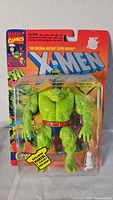 Front view of new in box X-Men Ch'od action figure showing green reptilian figure, red belt, and blue shorts in blister pack with Marvel Comics branding.