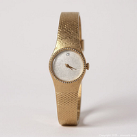 Front view showing gold-tone textured bangle watch with minimalist dial and beaded bezel
