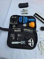 Open zip case displaying multiple watch repair tools and loose accessories