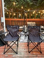 Two black Outbound branded outdoor camping chairs on wooden deck with string lights above, showing overall condition and appearance.