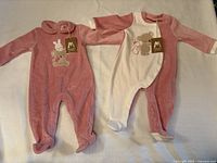 Two footed sleepers side by side, one pink and one white and pink with animal embroidery and tags attached.