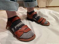 Side view of camel-colored genuine leather sandals on feet with socks, showing straps and buckle detail