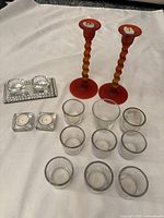 Photo showing red twisted candlesticks, the crystal duo tealight holder on mirror base, two square votive holders and multiple clear glass votive holders on white surface