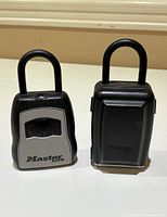 Two Masterlock lockboxes standing upright on a brown surface, showing front and back views.