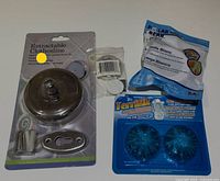 Photo showing a bundled lot containing a chrome retractable clothesline in packaging, two blue toilet cleaner tablets by Polar Bear, and a sealed pack of white V-strip weather tape.