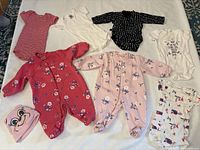 Overview of multiple newborn clothing pieces including bodysuits, sleepers, and a hat showing variety of colors and patterns.
