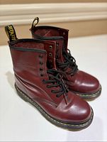 Front angled view of both oxblood Dr Martens lace-up boots showing smooth leather, black laces, and yellow stitching on sole.