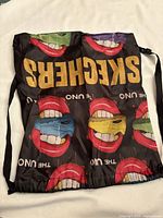 Black Skechers drawstring bag with colorful mouth patterns and gold Skechers logo, laid flat to show full design.