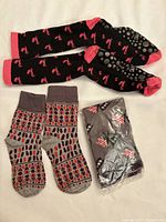 Three pairs of novelty sticky indoor socks. One black with red lobster pattern, one gray with geometric and mushroom patterns, one gray still in packaging with striped patterns. All have rubber like grip soles.
