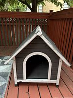 Front view of grey dog house with white trim and arched entrance on wooden deck.