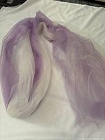 Sparkly lavender and cream tulle fabric loosely laid on a white fabric background showing two colors and sparkle texture.