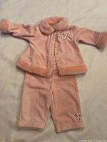 Pink vintage baby clothing set including jacket and pants laid flat on white surface.
