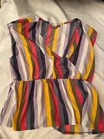 Photo of multicolor striped V-neck sleeveless blouse with gathered waist detail, laid flat.