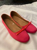 Top view of pink ballet flats with bow detail showing exterior and interiors on white background.