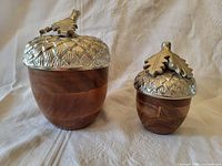 Photo showing both wooden jars with sculpted white brass acorn lids on top, side view