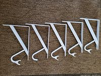 Five white metal shelf and rod brackets laid flat showing full length and hook design.