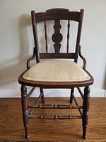 Front view of antique spindle wood chair with upholstered seat showing the carved detail on the backrest and turned legs.