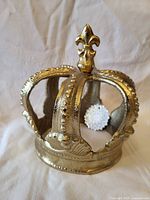 Front angled view of solid brass crown showing fleur-de-lis finial, textured finish, and raised dot details on arches.