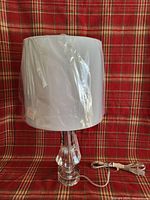 Full view of crystal lamp with white shade still wrapped in protective plastic on a plaid red background.