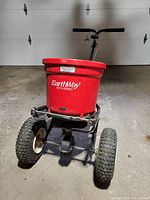Front view of the red EarthWay broadcast spreader showing the hopper and two front pneumatic wheels.