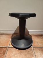 Side view photo of black wobble stool showing round base and octagonal seat with central support column.