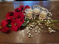 Sugar plum dreams faux poinsettia stems and pearl bead garlands laid on table, showing 9 red faux poinsettia stems and pearl bead garlands.