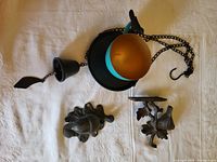 Top view showing hanging teacup birdfeeder, bell and iron bird bracket together on white cloth.