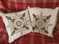 Pair of square cushions side by side on red plaid sofa, showing full snowflake beadwork pattern.