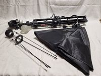 Folded light stand with bulb and socket, power cord, soft box folded beside it, and metal beams.