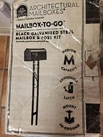 Box label showing Architectural Mailboxes MAILBOX-TO-GO black galvanized steel mailbox kit, medium capacity, adjustable latch, in-ground mount.