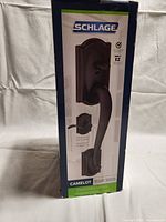 Front view of the Schlage Camelot FE285D handle set packaging showing the product image and branding in aged bronze finish.